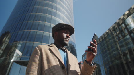 Black-Businessman-Standing-Outdoors-in-Downtown-and-Using-Smartphone